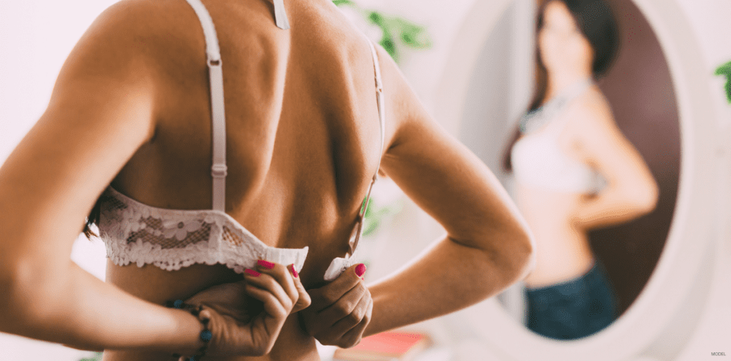 A woman looks in the mirror at her breast augmentation results.